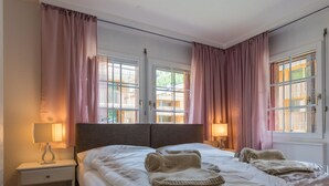 A hotel room with two beds, a nightstand, a lamp, and a window with curtains. - Casa Antares – Montela Holiday Stay by Interhome (Saas-Grund)