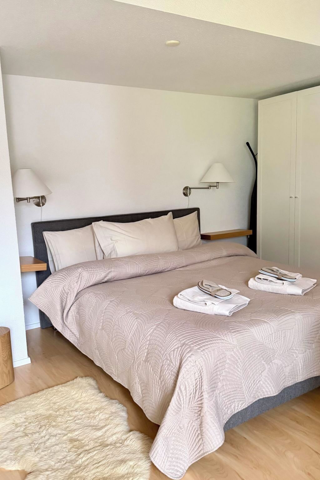 A bedroom with a bed, two wall-mounted lamps, a wardrobe, and a fluffy rug.