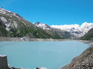 A mountain landscape with a clear blue lake, rocky terrain, and snow-capped peaks.