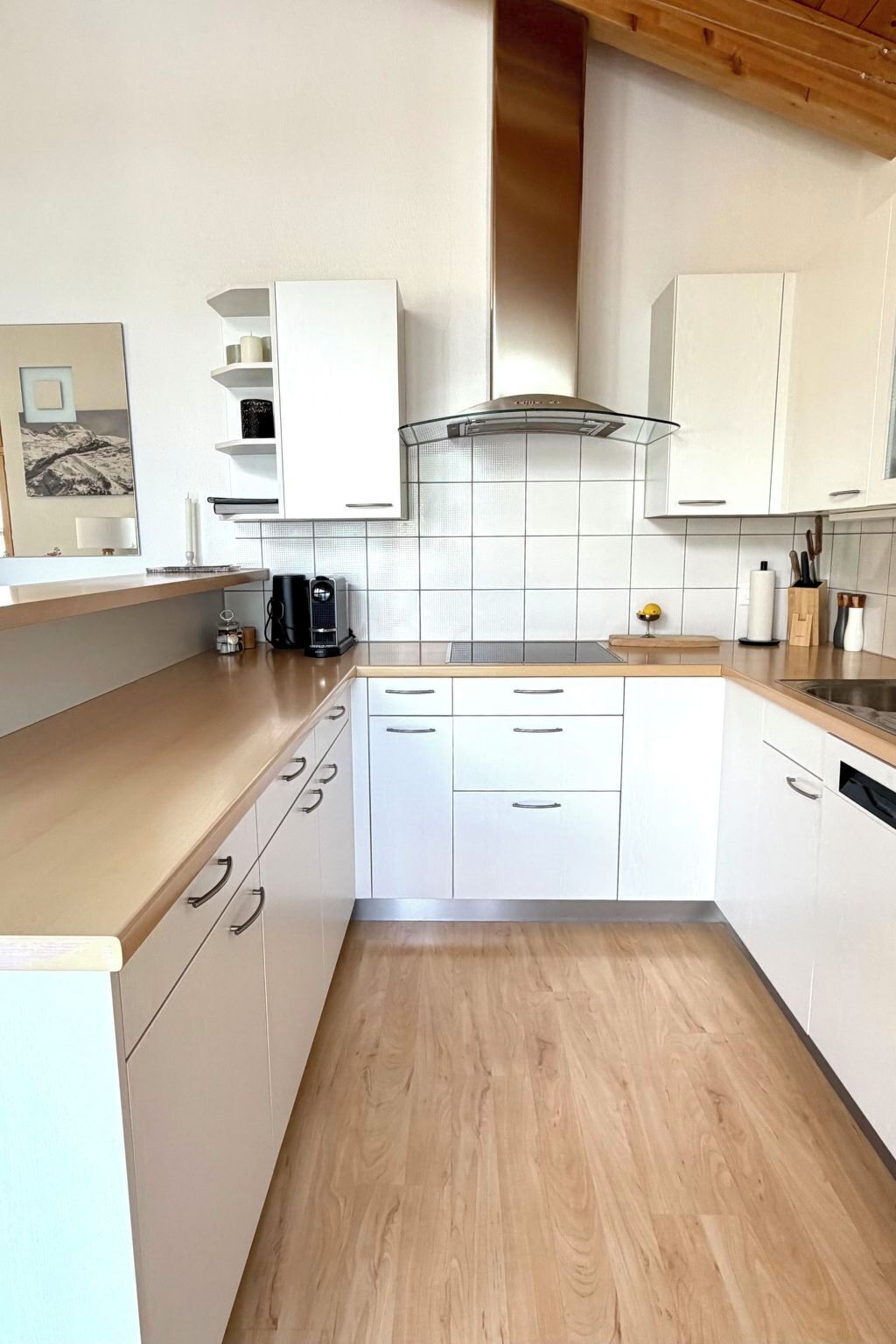 A modern kitchen with white cabinets, a wooden countertop, and a stainless steel range hood.