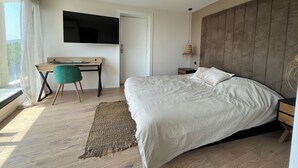 Un dormitorio con cama, escritorio, silla, televisor y ventana con cortinas.