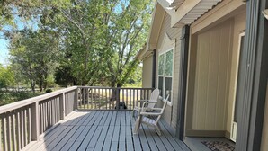 A wooden deck with a railing, two Adirondack chairs, and a door to a covered porch. - Relax after a Day on the Lake! (Hulbert)