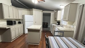 A compact kitchen with white cabinets, a refrigerator, a microwave, and a striped table. - Relax after a Day on the Lake! (Hulbert)