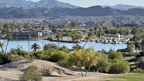 Um campo de golfe com um corpo d'água e montanhas ao fundo.