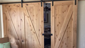 Quarto com porta de correr estilo rústica, sofá de vime com almofada verde e ventoinha no teto.