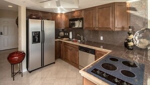 Uma cozinha com armários de madeira, geladeira de aço inoxidável, micro-ondas, lava-louças e bancada de granito.