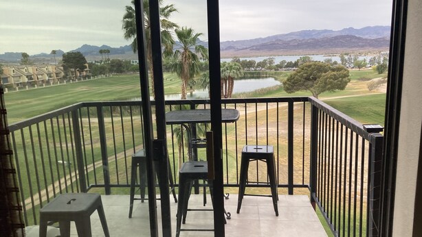 Uma varanda com vista para um campo de golfe, palmeiras e montanhas ao longe.