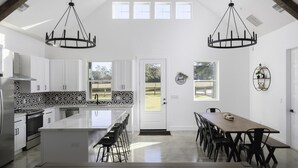 Una cocina amplia con una isla central, muebles blancos y un ventanal grande.