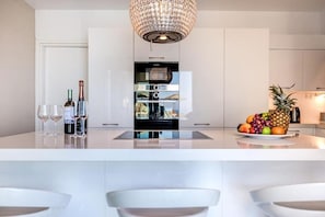Una cocina moderna con una isla central, copas de vino, botellas y un frutero.