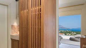Un intérieur moderne avec un mur lambrissé en bois, une salle de bain dotée d’un plan de toilette en marbre et une vue sur la mer et les bâtiments.