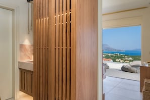 A modern interior with a wooden panel wall, a bathroom with a marble countertop, and a view of the sea and buildings.