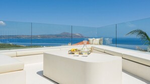 Un espace extérieur moderne, aménagé pour se détendre, offrant une vue dégagée sur la mer et sur une chaîne de montagnes lointaine.