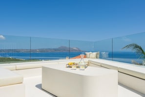 A modern outdoor seating area with a clear view of the sea and a distant mountain.