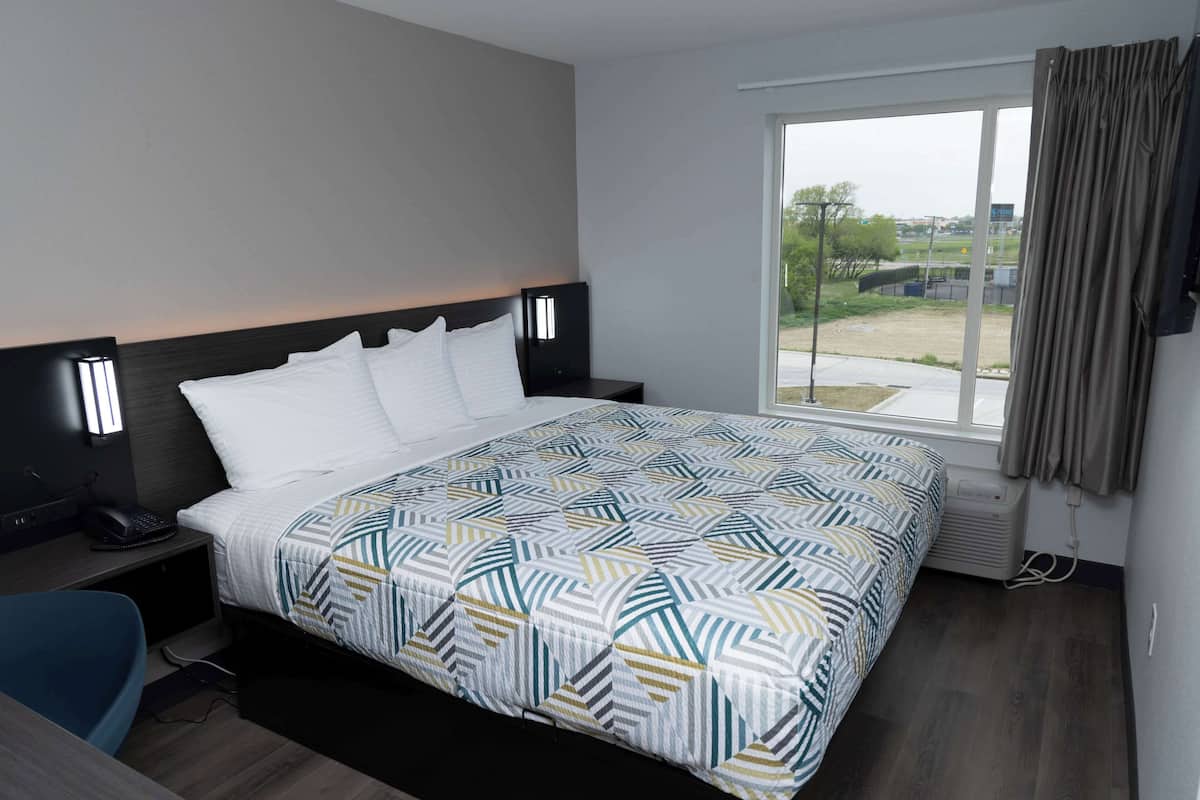 A hotel room with a bed, a desk, a chair, a window with curtains, and a view of the outside.