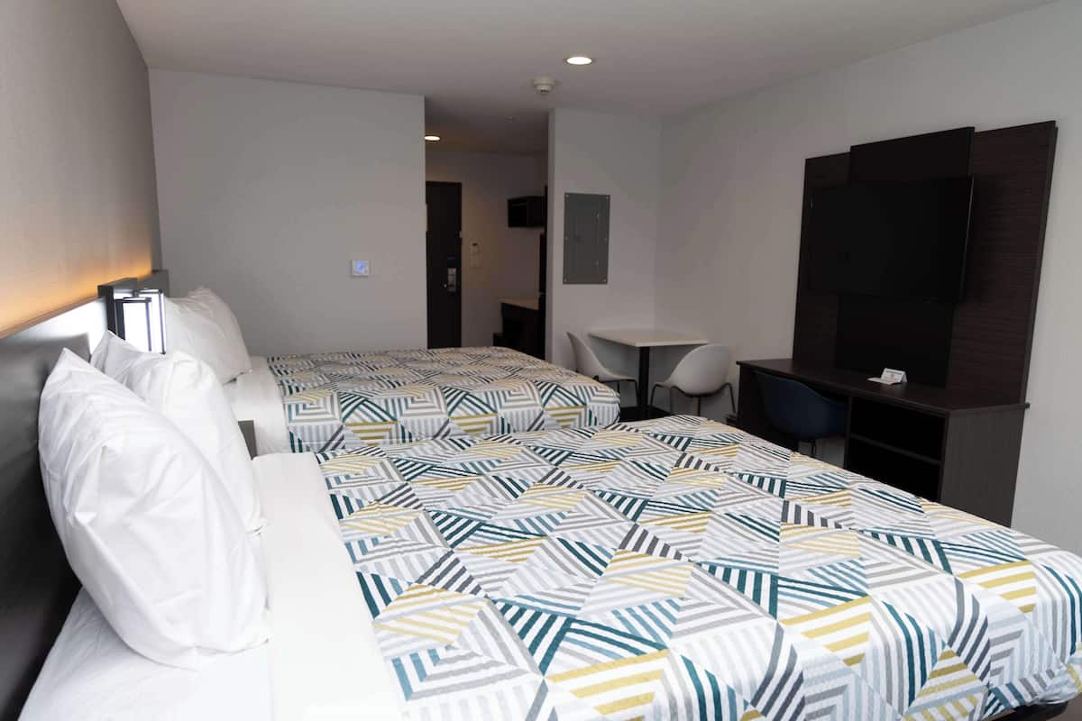 A hotel room with two beds, a desk, a chair, a TV, and a small table.