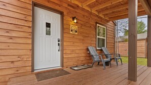 A wooden cabin with a white door, a porch with two chairs, and a small sign on the wall. - Cabin # 3 at Northern Comfort w/opt side by side rentals (Atlanta)
