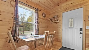 A wooden cabin interior with a dining table, chairs, a window with curtains, a door, and a wall clock. - Cabin # 3 at Northern Comfort w/opt side by side rentals (Atlanta)