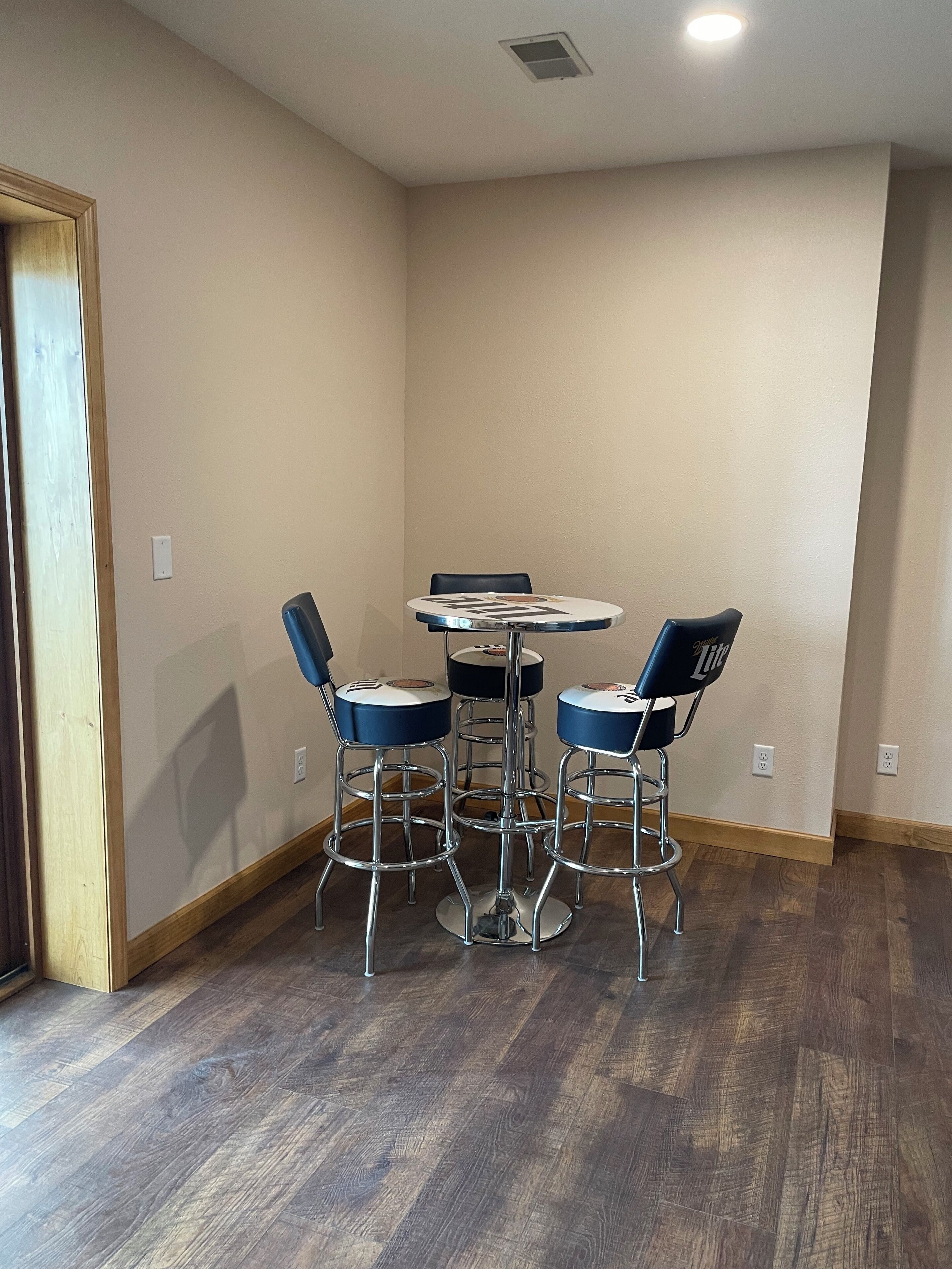 Une pièce avec un plancher en bois, une petite table ronde à plateau blanc et quatre chaises bleues, et des murs de couleur beige.