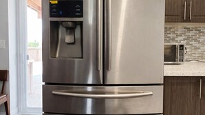 A stainless steel Samsung refrigerator with a water dispenser, located in a kitchen with wooden cabinets and a tiled backsplash.
