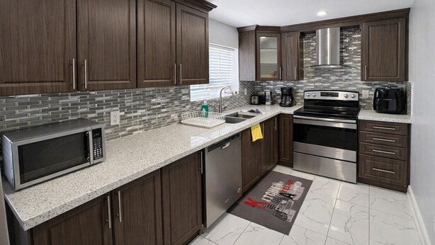 A modern kitchen with dark wood cabinets, stainless steel appliances, and a tiled backsplash.