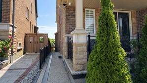 A residential building with a stone facade, a covered porch, and a well-maintained garden with a coniferous tree.
