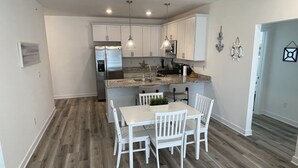 A modern kitchen with white cabinetry, a stainless steel refrigerator, a granite countertop, and pendant lighting. - Condo on Rehoboth Bay close to beaches and boating (Lewes)
