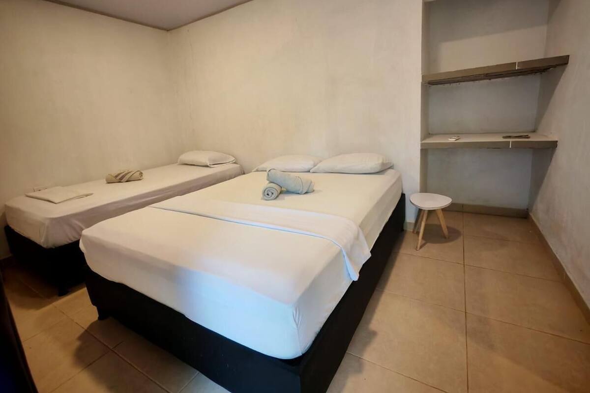 A room with two beds, a small stool, and a shelf unit.