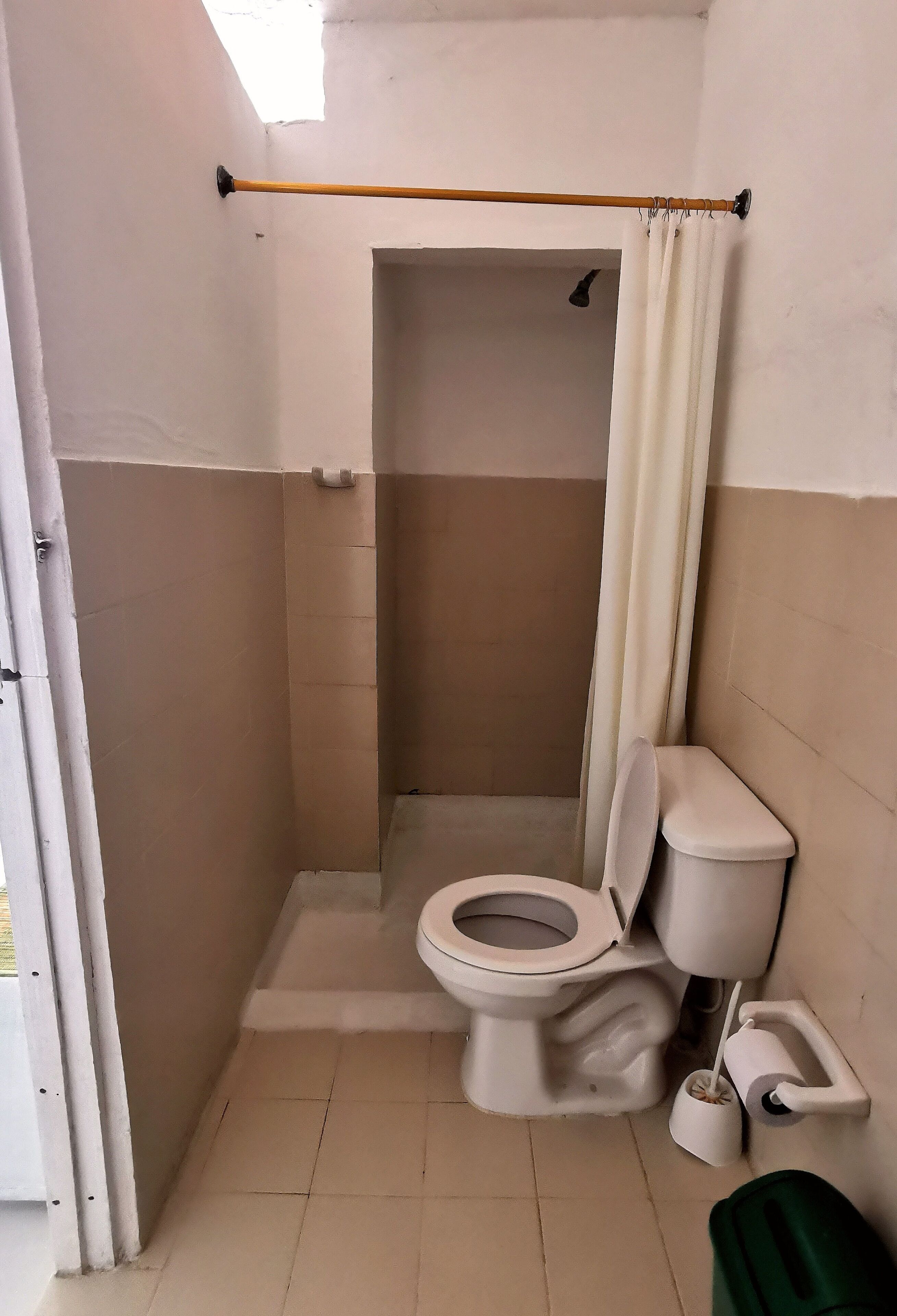 A small, enclosed bathroom with a toilet, a shower area, and a curtain rod.