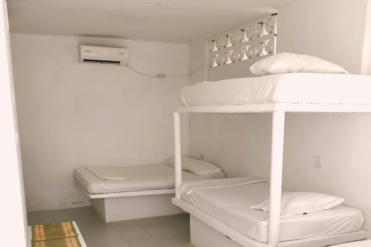 A bunk bed room with a white air conditioner, a small table with a patterned tablecloth, and a tiled floor.