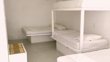 Quarto com beliche, ar condicionado branco, uma pequena mesa com toalha de mesa estampada e piso ladrilhado.