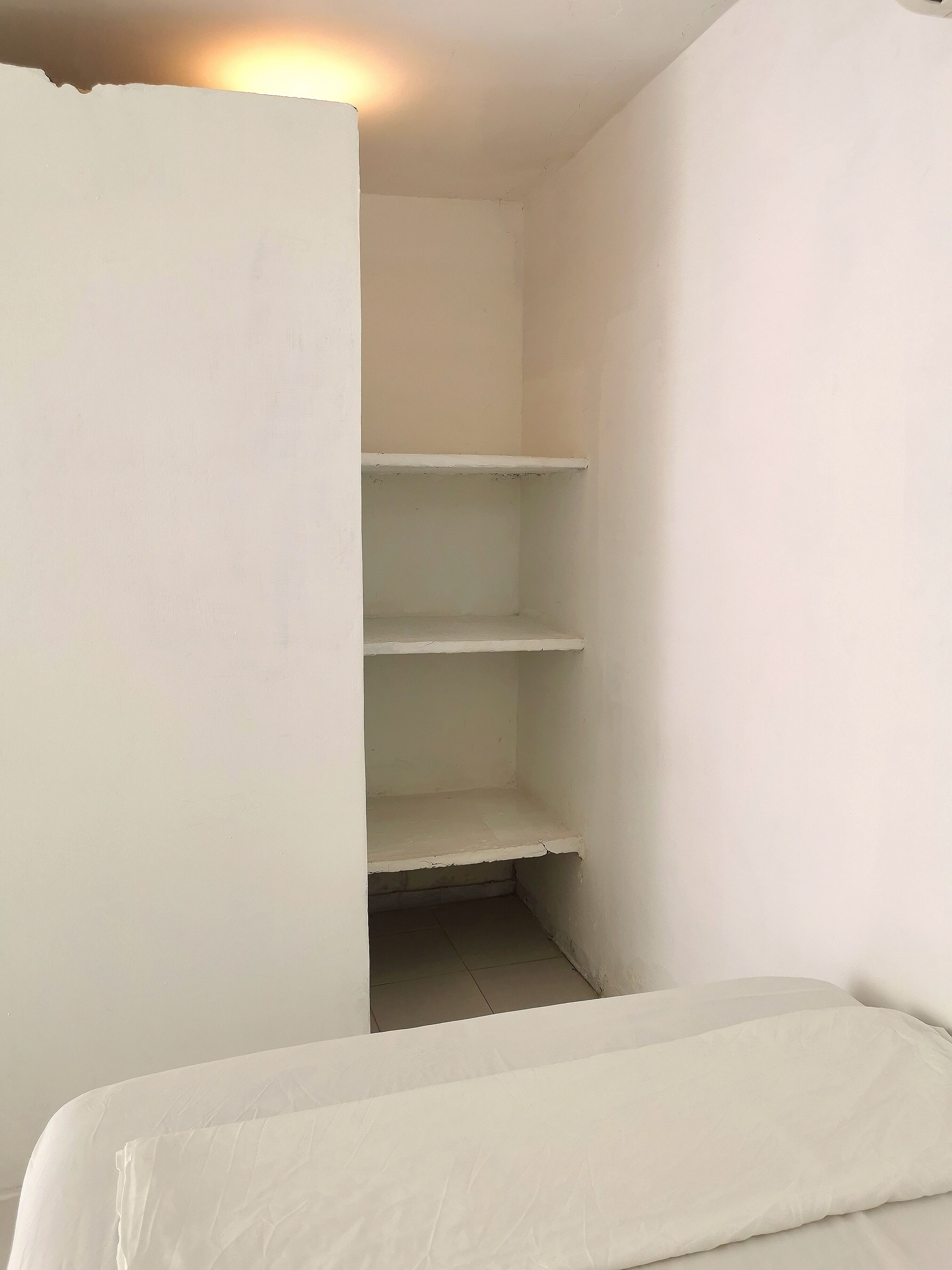 Une petite pièce blanche, avec un lit et trois étagères blanches.