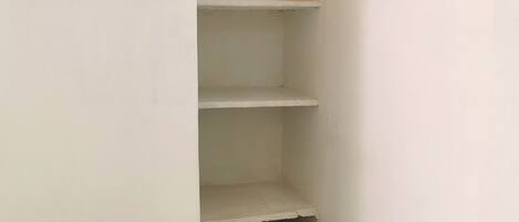 Une petite pièce blanche, avec un lit et trois étagères blanches.