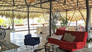 Un espace extérieur abrité, doté d’un toit de chaume, d’un canapé rouge, d’une chaise bleue et d’un tapis en peau de vache.