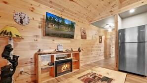 Un intérieur en bois avec une cheminée, une horloge, un téléviseur et un réfrigérateur.