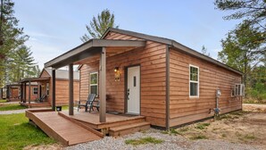 Une cabane en bois dotée d’un porche couvert, d’une porte et d’un petit espace extérieur aménagé pour s’asseoir.