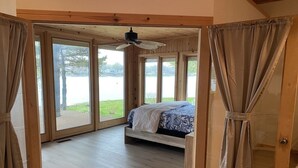 Een slaapkamer met een bed, een plafondventilator en grote ramen met uitzicht op een meer.