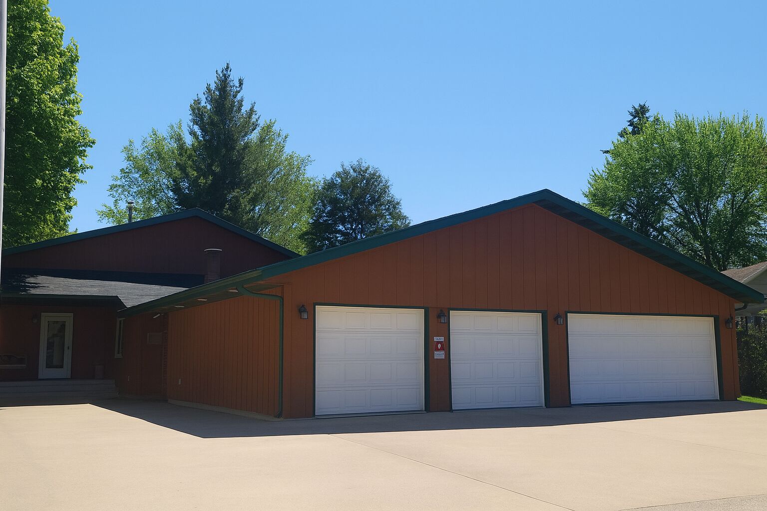 A two-story building with a brown exterior and a green roof. It has three garage doors and a small entrance with a door.