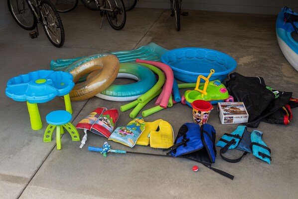 A collection of inflatable toys and a blue kayak on a concrete floor.