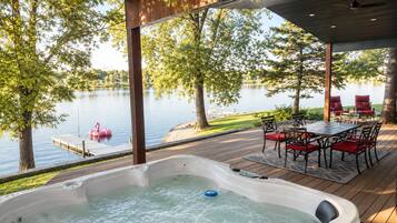 Ein Whirlpool auf einer Holzterrasse mit Blick auf einen See und eine Anlegestelle mit einem Flamingo-Schwimmschwan.