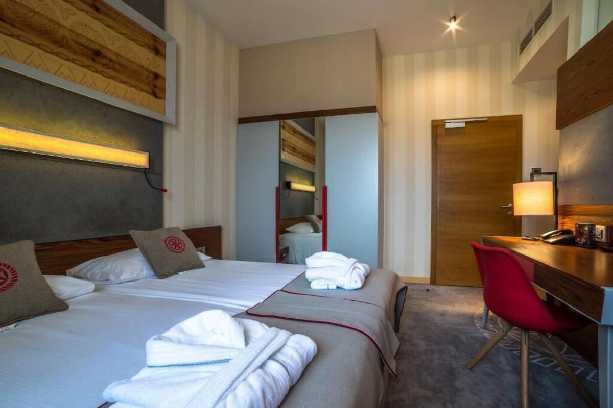 Una habitación de hotel con dos camas, un escritorio, una silla roja y un espejo.