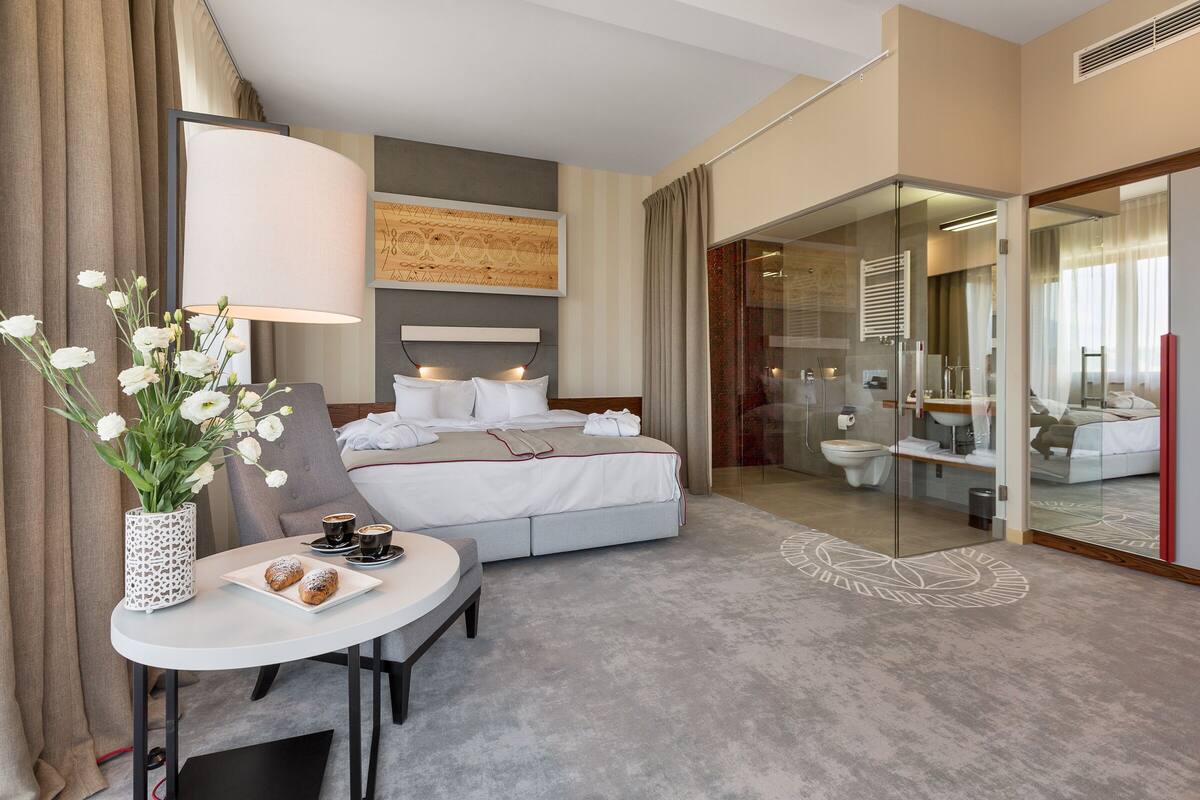 Una habitación de hotel moderna con una cama, un escritorio con una lámpara, un jarrón con flores y una bandeja de desayuno.