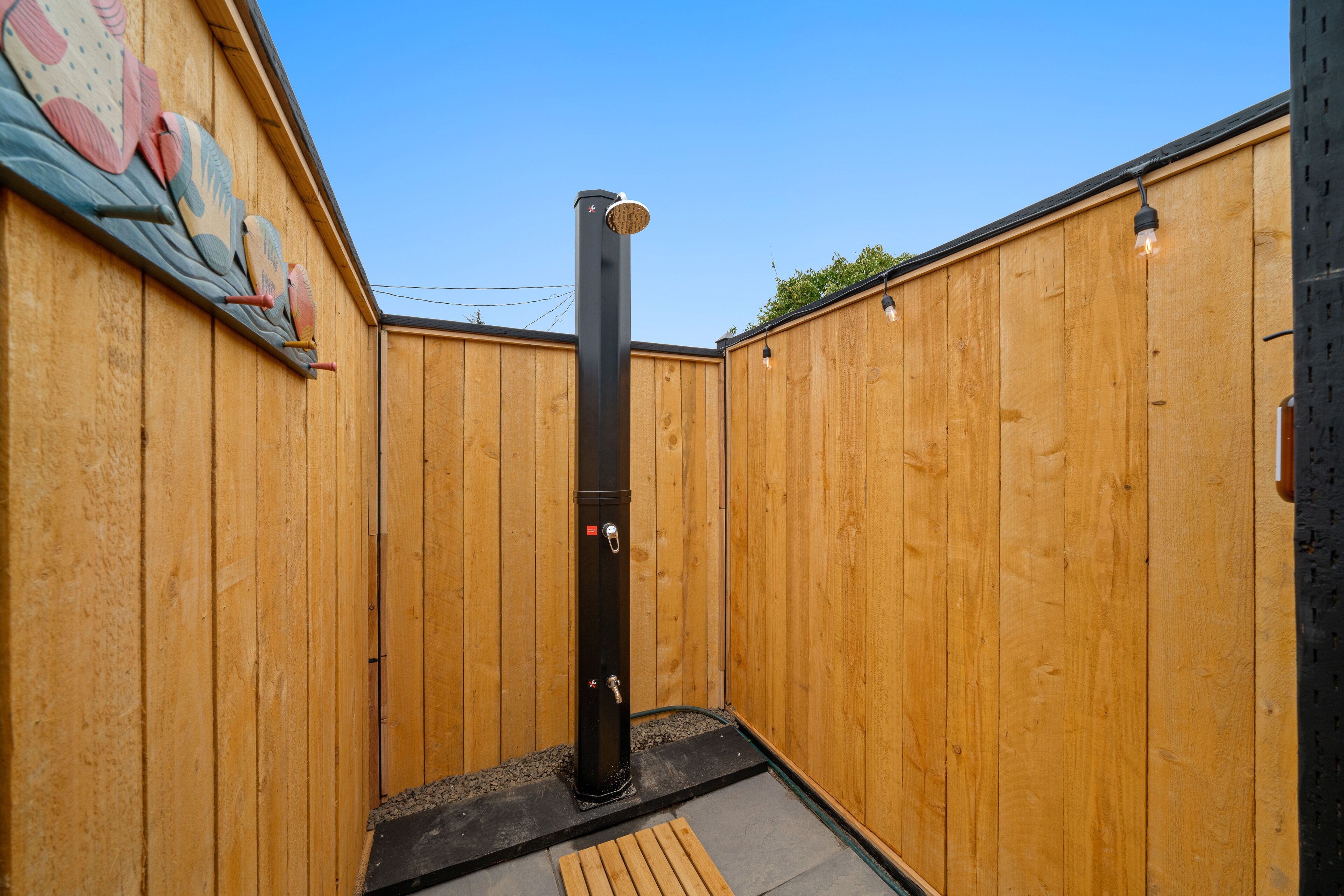 A wooden fence enclosure with a black vertical structure, possibly a sauna or hot tub, and a light fixture on the right.