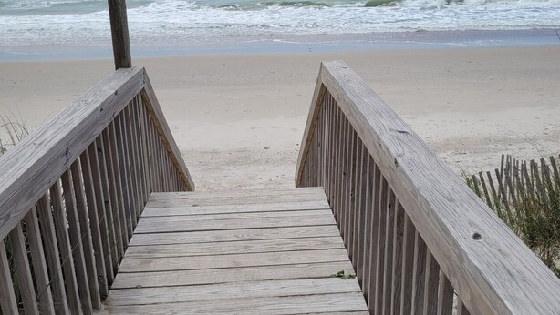 Pasarela de madera que conduce a una playa, con olas al fondo.