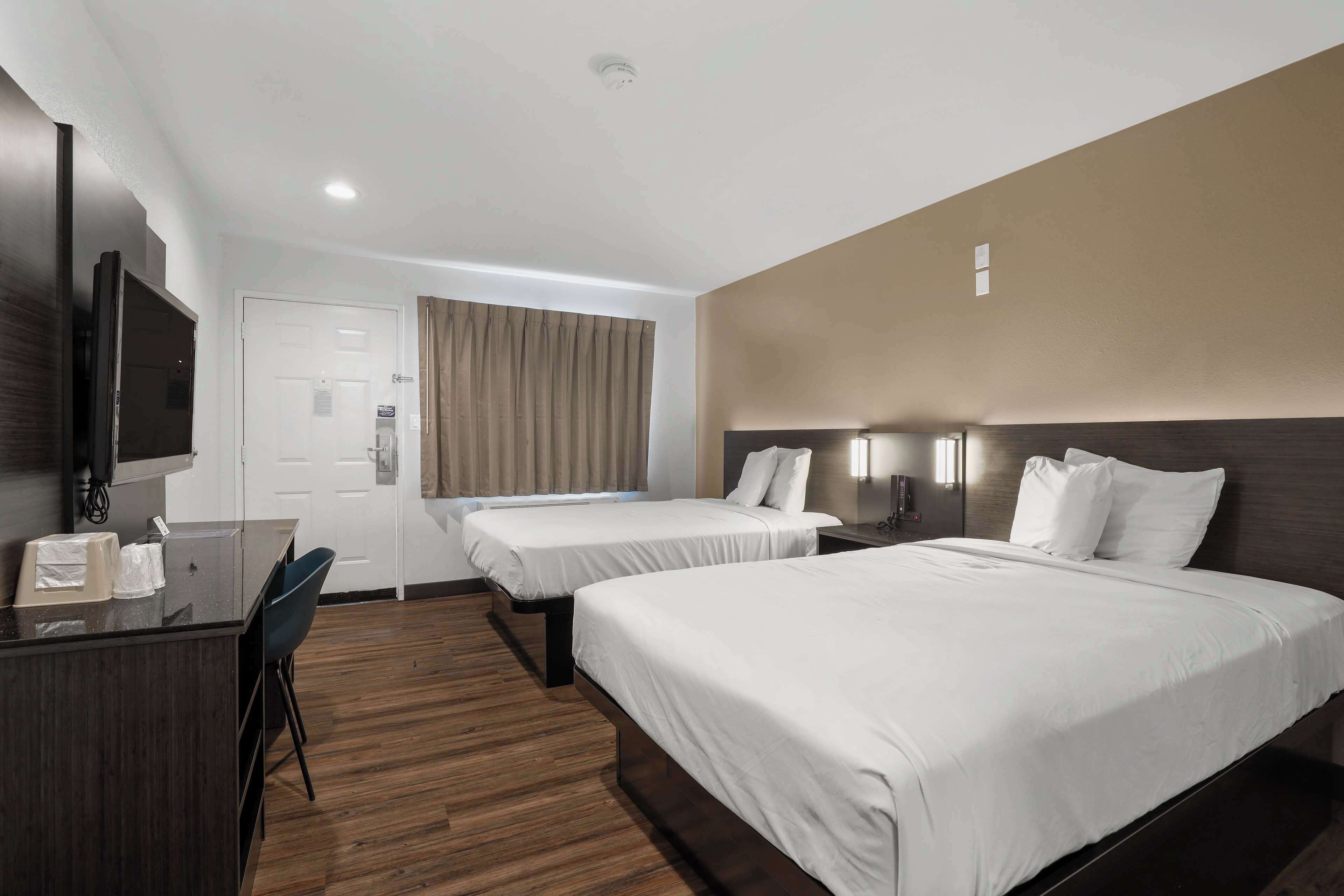 A hotel room with two beds, a desk, a chair, a TV, and a window with curtains.