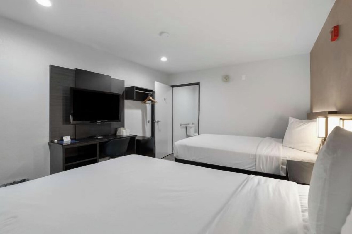 A hotel room with two beds, a desk with a flat-screen TV, and a wardrobe.