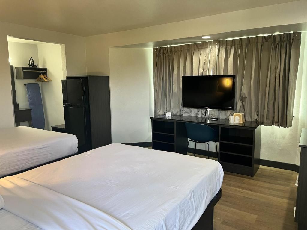 A hotel room with two beds, a desk with a flat-screen TV, a chair, and a wardrobe.