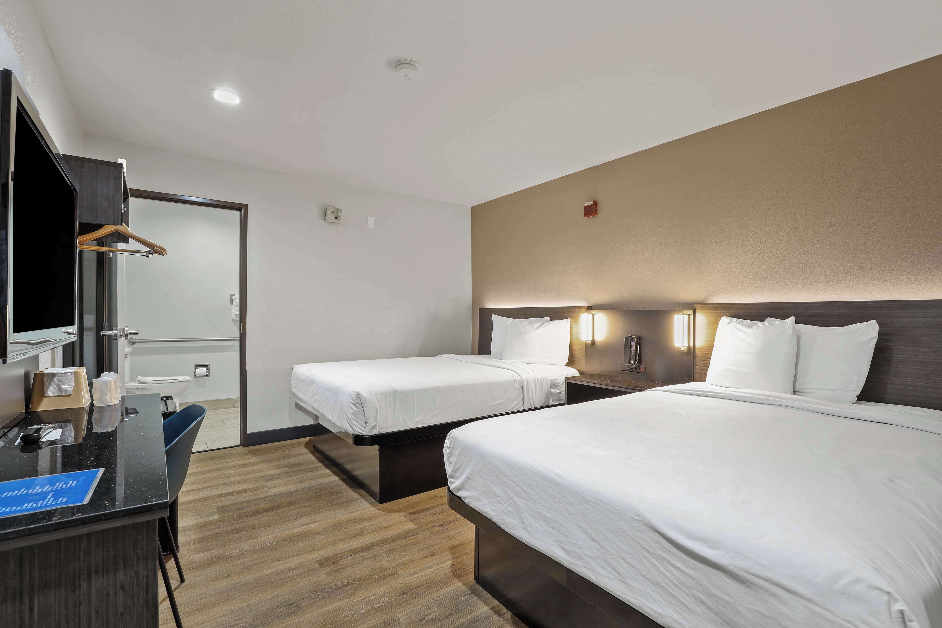 Una habitación de hotel con dos camas, un escritorio, un espejo y un armario.