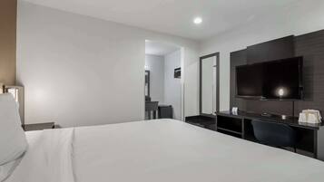 Una habitación de hotel con cama, escritorio, silla, televisión de pantalla plana y espejo.