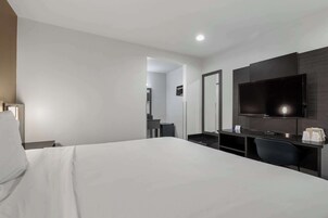 Una habitación de hotel con cama, escritorio, silla, televisión de pantalla plana y espejo.