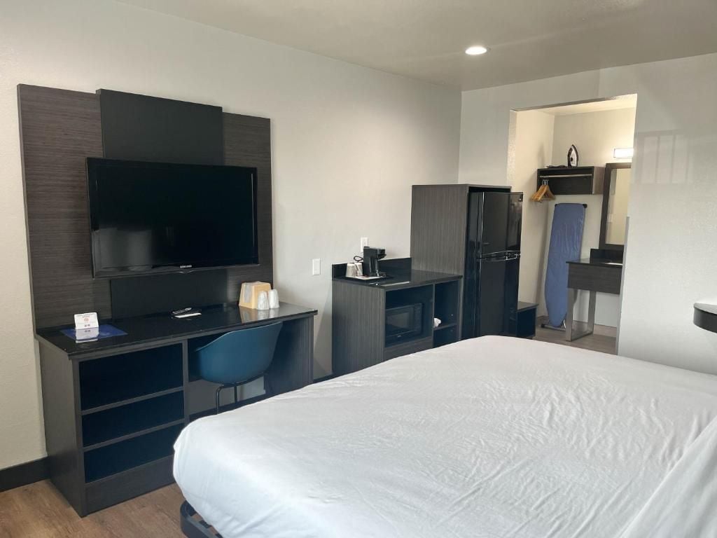 Een hotelkamer met een bed, een bureau met stoel, een televisie, een kledingkast en een badkamer zichtbaar door een geopende deur.